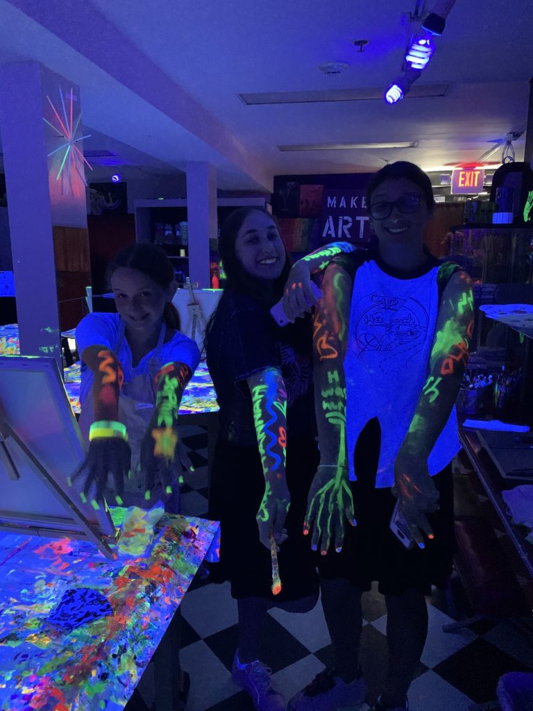 Three people with glow-in-the-dark paint on their arms enjoying a vibrant neon atmosphere at a Glow Party in Englewood, NJ.